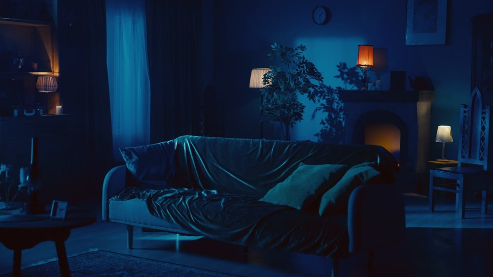 Dim bedroom at night with blue moonlight from a window falling on a bed and a nightstand with a lamp